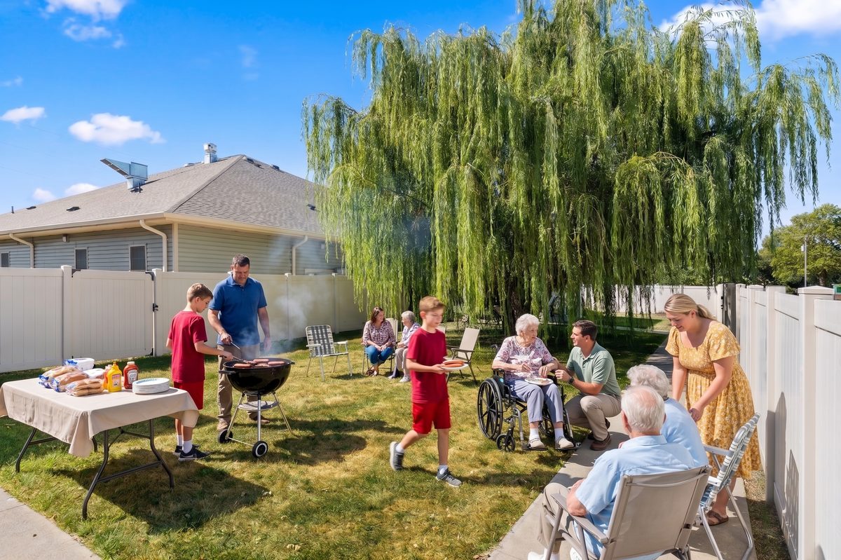 Residents, caregivers, and young volunteers enjoying a cookout under the willow tree